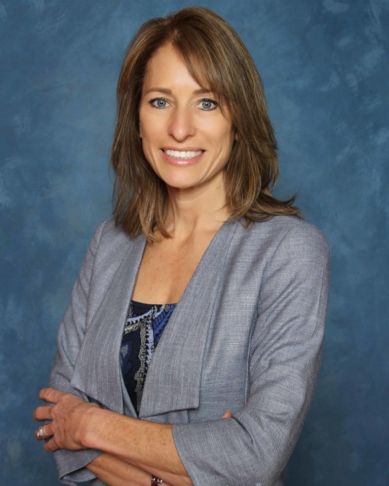 A smiling woman in a gray suit and blue shirt.